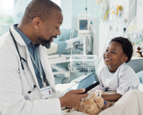 Side view of a doctor talking to smiling little boy while sitting on hospital bed